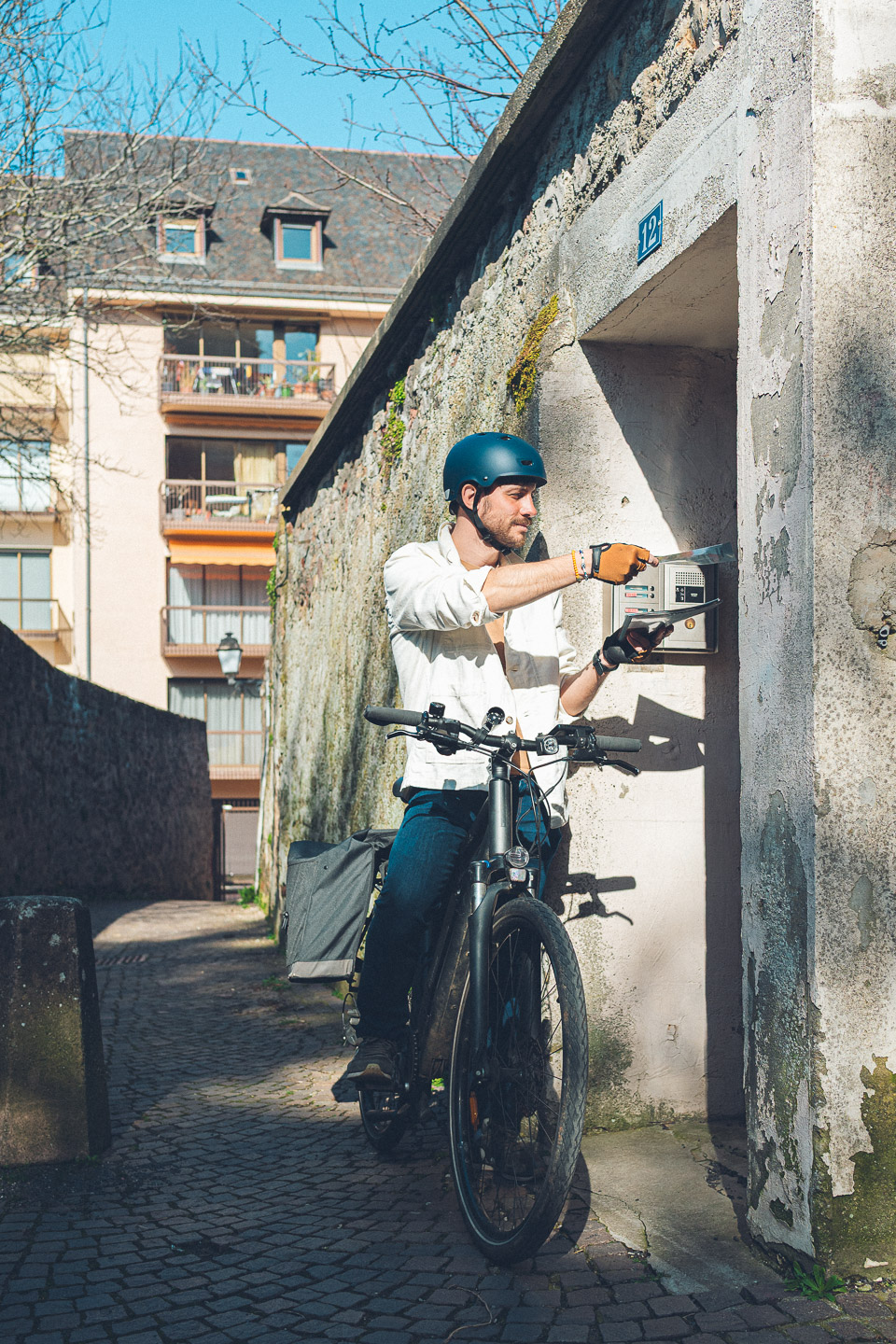 Pierre-Étienne dépose un document dans une boîte aux lettres, à vélo, dans une ruelle de Rodez