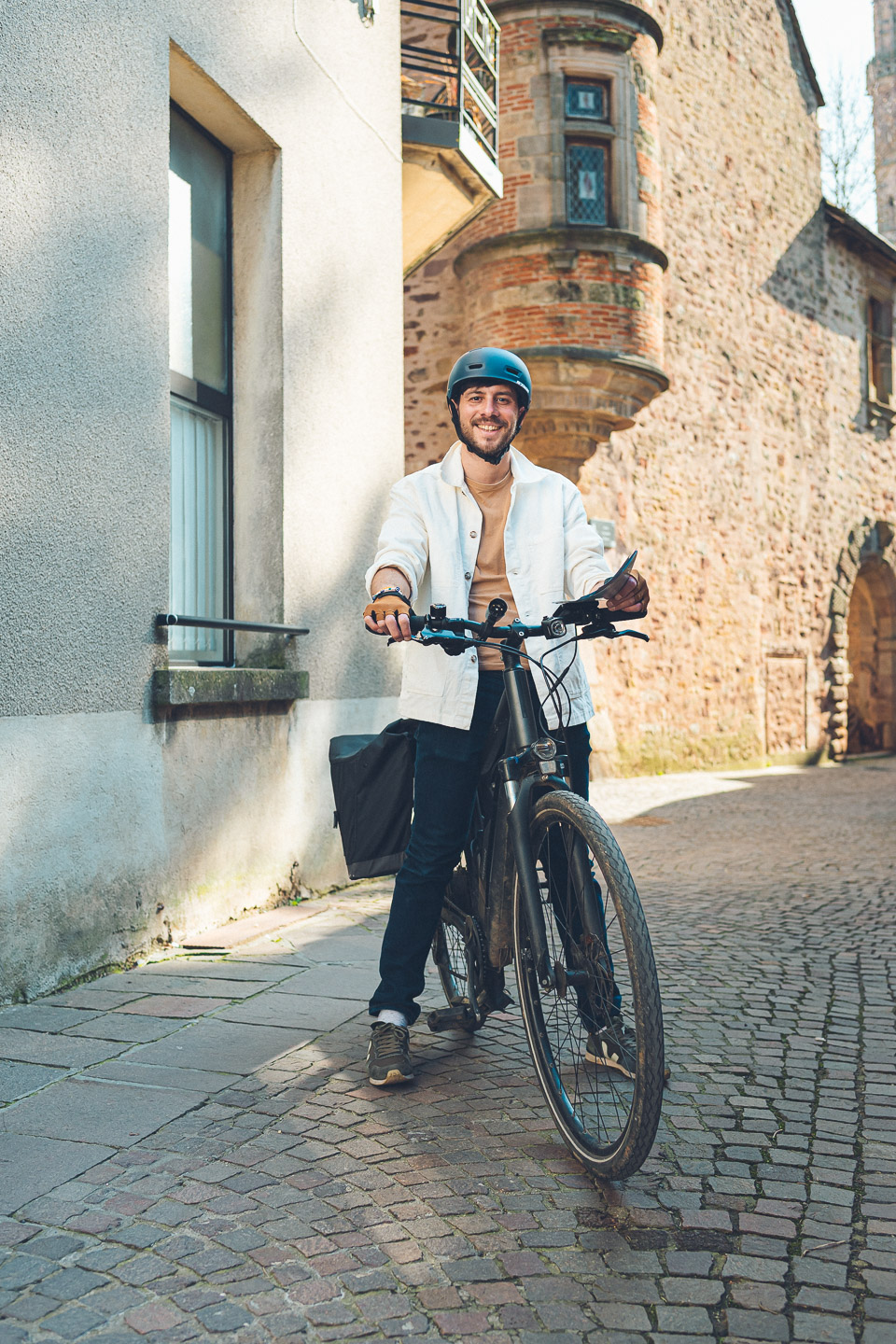 Pierre-Étienne souriant sur son vélo électrique devant une maison en pierre de Rodez